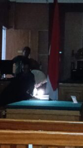 JPU Siti baca visum et repertum dengan cara menyalakan lampu senter dari ponselnya. (Sumber foto: JP - BatamPena.com)