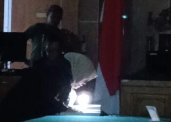 JPU Siti baca visum et repertum dengan cara menyalakan lampu senter dari ponselnya. (Sumber foto: JP - BatamPena.com)